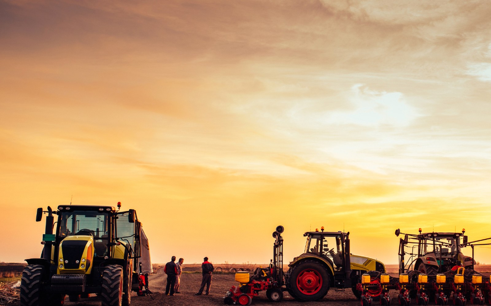 Tractors and seeding rigs lined up in a paddock at sunset